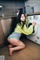 A woman sitting on the floor next to a washing machine.