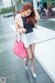 A woman walking down a sidewalk carrying a pink bag.