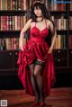 A woman in a red dress standing in front of a bookshelf.