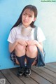 A young woman in a school uniform sitting on a wooden floor.