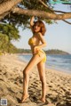 A woman in a yellow bikini standing on a beach.