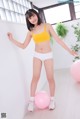 A woman in a yellow top and white panties standing next to a pink ball.