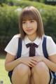 A young woman in a school uniform sitting on the grass.