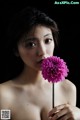 A woman holding a pink flower in her hand.