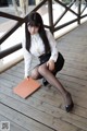 A woman in a white shirt and black skirt sitting on a wooden floor.