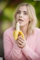 A woman in a pink sweater holding a banana in her mouth.