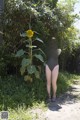 A woman in a black bathing suit standing next to a sunflower.